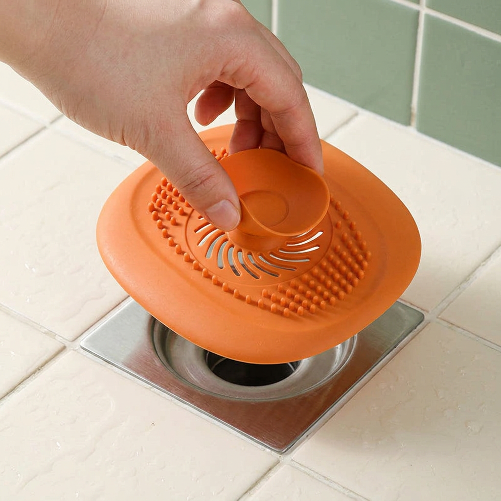 Adult lifting an orange hair catcher from a shower floor drain
